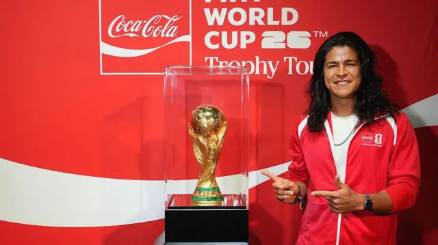 Cristo Fernández, viste una sudadera roja y está al lado del trofeo FIFA de la Compa Mundial