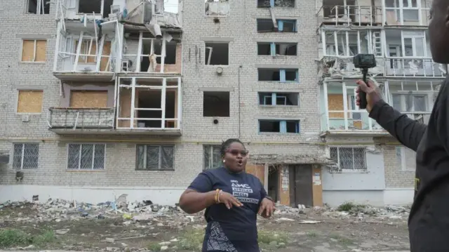 Ivy Setordjie em frente a um prédio destruído.