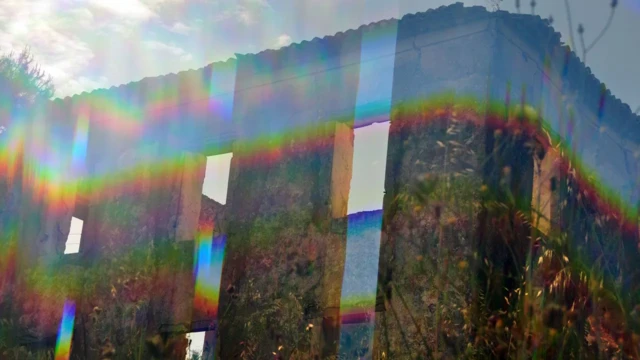 건물과 땅과 풀이 어지럽게 뒤섞이고 그 위로 무지갯빛이 비치는 모습