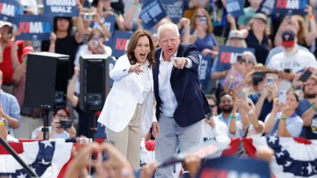 Kamala está ombro a ombro com Tim Walz, um homem branco,joguinho que ganha dinheirocabelos brancos. Ambos estão apontando o indicador para a foto, cercadosjoguinho que ganha dinheiroapoiadores.