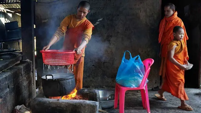 Três jovens monges preparam comida no fogo