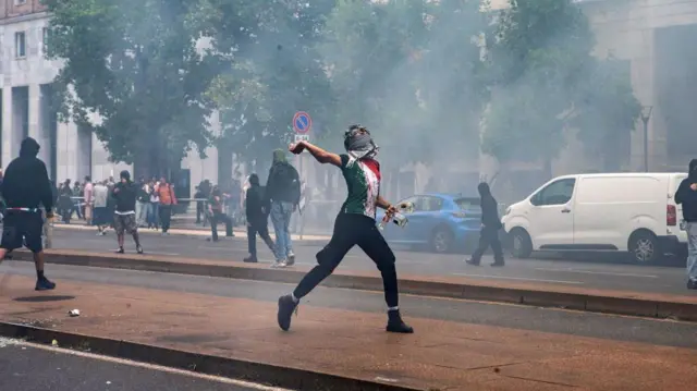 Mladić lica prekrivenog maramom baca kamen