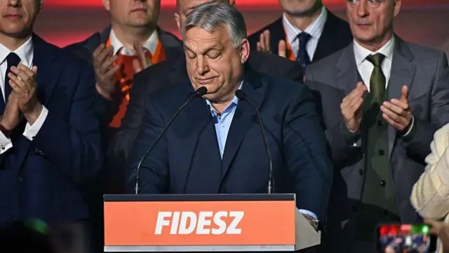 オルバン氏がフィデス(FIDESZ)と書かれた演台でマイクを前に目を伏せて口を閉じている。背後ではスーツ姿の人々が拍手している