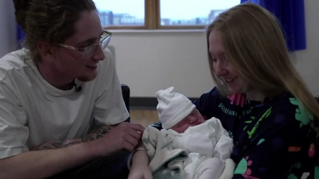 Sonny y Holly se sientan juntos sosteniendo a un bebé recién nacido envuelto en una manta