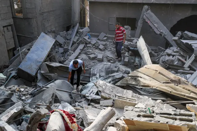 فلسطينيون يتفقدون موقع غارة جوية إسرائيلية في مدينة غزة