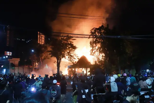 মোটর সাইকেল নিয়ে ও রাস্তায় দাঁড়িয়ে পেছনে আগুনের দৃশ্য দেখছেন অনেকে