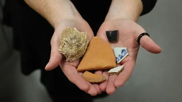 Un primer plano de un par de manos que sostienen fragmentos de cerámica marrón, blanca y negra de diferentes tamaños.