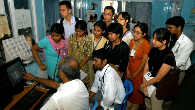 Les étudiants se rassemblent près de leur professeur qui explique quelque chose en pointant son écran.