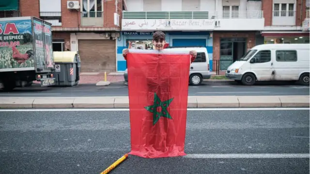 Boy with a large Moroccan flag standing in the street.