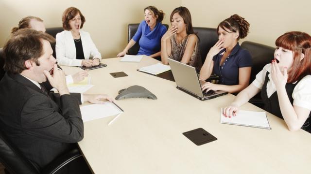 Un grupo de personas sentadas alrededor de una mesa de oficina bostezando