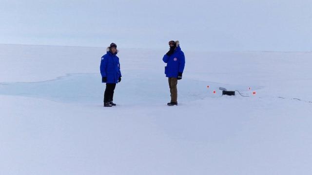 Dos investigadores envueltos en equipo ártico mientras observan la bomba de agua de mar en acción.