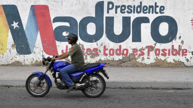 Un motociclista pasa frente a un miro con un mensaje de apoyo a Maduro.