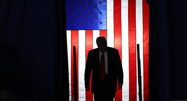 الرئيس الأمريكي، دونالد ترامب واقفاً ويرتدي سترة زرقاء وقميصاً أبيض وربطة عنق حمراء.