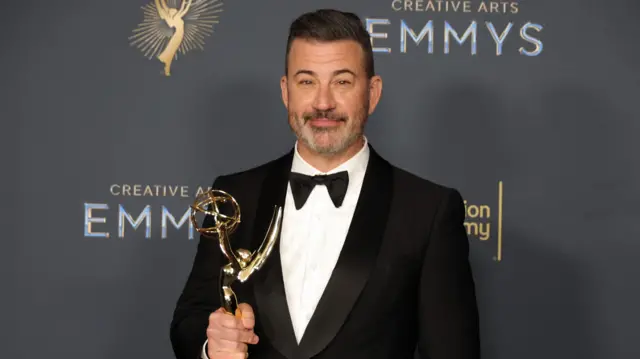 Jimmy Kimmel sostiene una estatuilla de los Emmy mientras luce un esmoquin y mira a la cámara