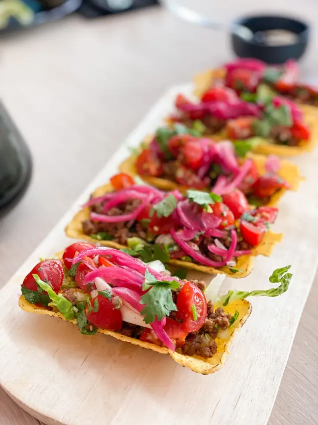 Un plato largo de madera con una fila de tacos servidos sobre él