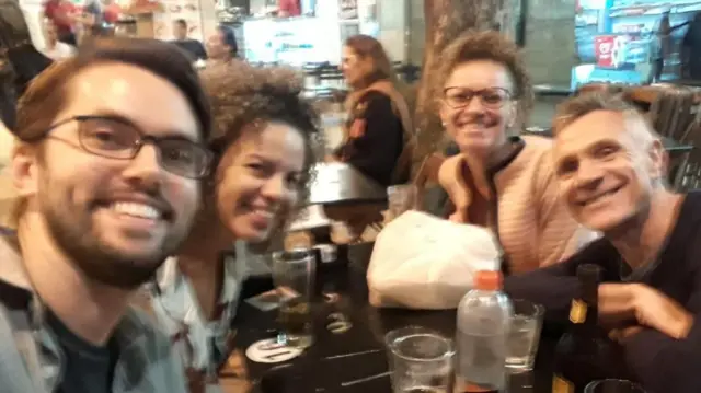 Une photo légèrement floue d'un groupe d'amis assis autour d'une table en train de manger et souriant à l'appareil photo.