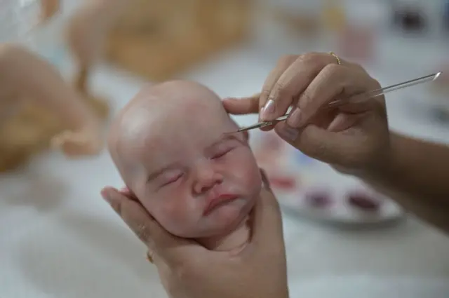 A mão de uma artesã pinta detalhes de uma cabeça de uma boneca bebê super realista em seu ateliê em Contagem, Minas Gerais, em 16 de novembro de 2021