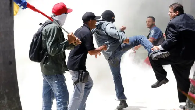 Hombre enmascarado golpea a otro hombre de traje.