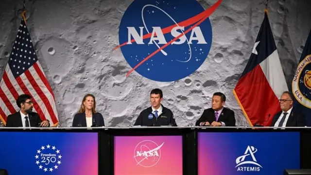 月面のイメージやNASAのマーク、アメリカの国旗などを背に、記者会見するNASA幹部