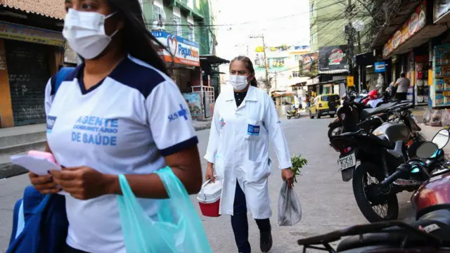 Duas mulheres com máscaras faciais e uniformes de saúde caminham em rua