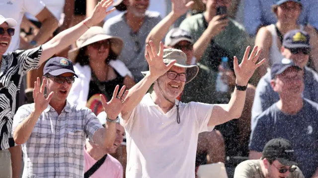 Kibice na trybunach French Open cieszą się wodą ze zraszaczy. Na pierwszym planie dwóch uśmiechniętych mężczyzn z uniesionymi rękami