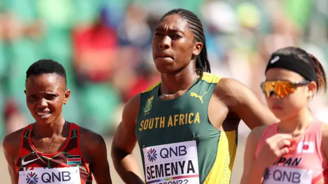 Caster Semenya, con dos atletas, a sus lados, en un estadio de atletismo.