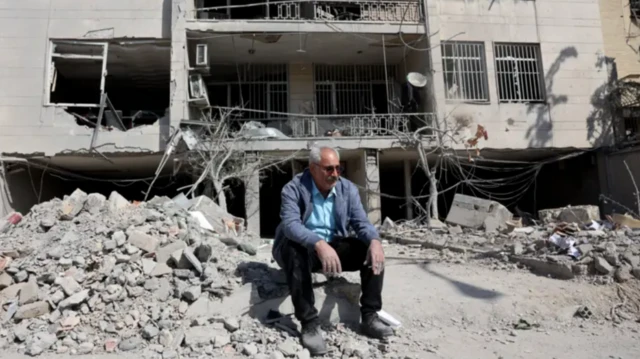 Tehranda dağılmış bina önündə oturan kişi