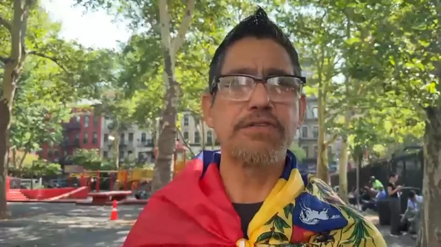 Un hombre con cabello corto y barba recortada. Lleva anteojos y tiene colocada sobre sus hombros una bandera de Venezuela.