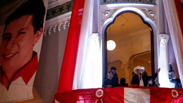 à noite, Castillo aparece na sacada de um prédio histórico falando ao microfone, com bandeiras do Peru e grande foto sua em volta