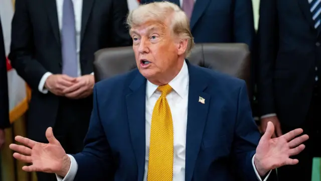 ダークスーツに金色のネクタイを着けたトランプ米大統領が、大統領執務室の椅子に座り、両手を広げて話をしている
