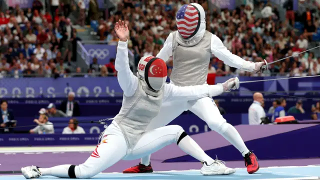 A fencer in mask with a Singapore flag on it competes with an athletes with a US flag on his mask