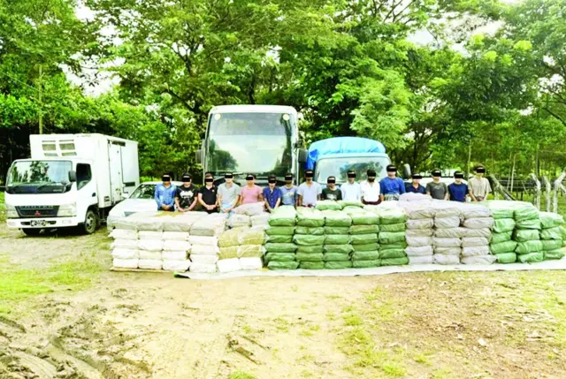 ကား၃ ဦးရဲ့ အရှေ့မှာ ရပ်နေတဲ့ အမျိုးသား ၁၆ ဦး သူတို့ရဲ့ ရှေ့က မြွေရေခွံအိတ် အဖြူရောင် အစိမ်းအထုပ်များ 