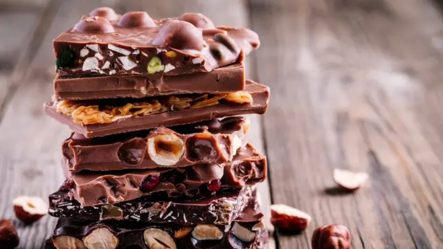 කොකෝවා,චොක්ලට් A stack of chocolate bars, some containing nuts, sitting on a wooden table