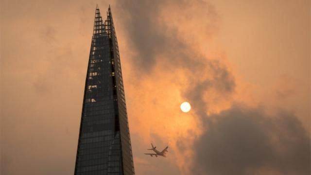 Un avión vuela por el edificio Shard en el centro de Londres, mientras el cielo muestra un color naranja inusual.
