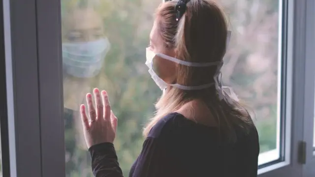 Mulher com máscara olhando na janela