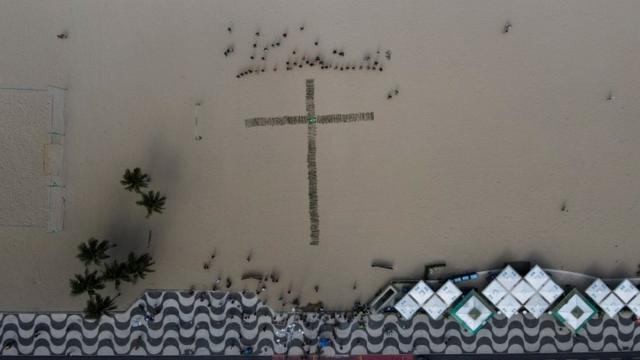 Foto áerea mostra cruz formada por rosas na areia da praia de Copacabana