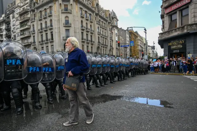 Jubilado camina al lado de una fila de policías 