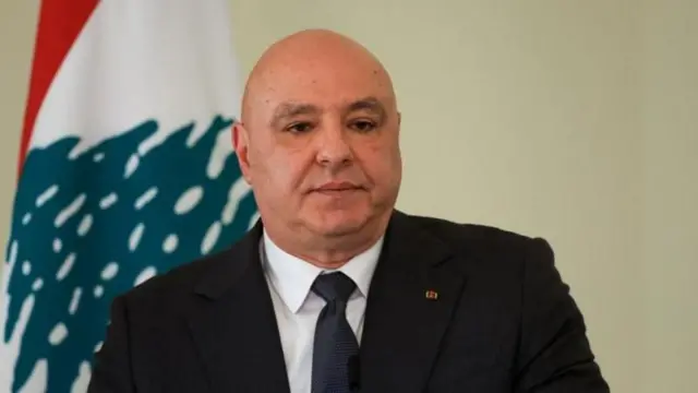 Lübnan Cumhurbaşkanı resmi giyisili ülkesinin bayrağı önünde duruyor. 