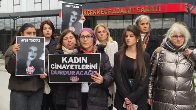 Dokuz kadın bir arada. Arkada Küçükçekmece Adalet Sarayı var. İki kadın ellerinde Ayşe Tokyaz'ın fotoğrafını tutuyor. Bir kadın da üzerinde Kadın Cinayetlerini Durduracağız yazılı bir karton tutuyor.