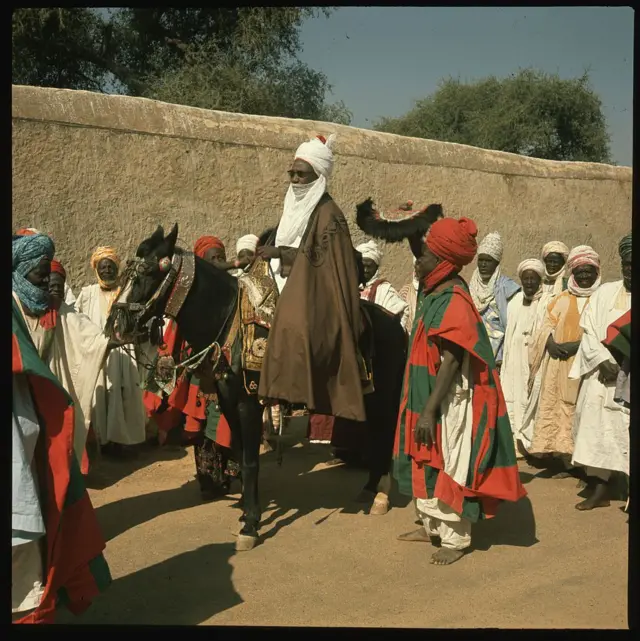 Sarkin Kano Alu Maisango haye a kan doki bisa rakiyar dogarai a 1899.