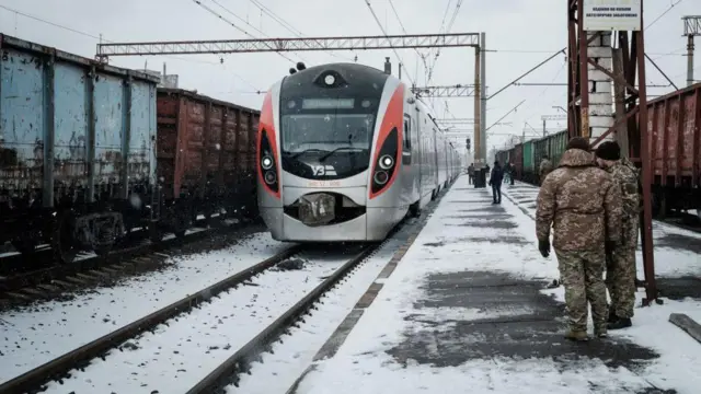 Потяг прибуває взимку на станцію, на пероні стоять військові 