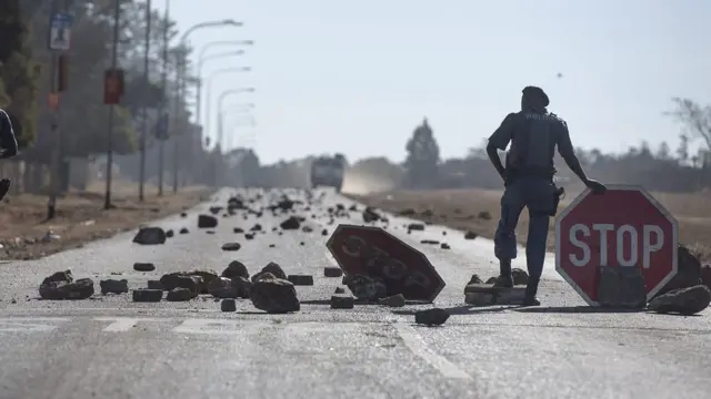South African police forces stand at a barrier of stones made by protesters during an ongoing service delivery protest south of Johannesburg, South Africa - Saturday 23 July 2016