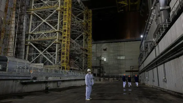 Работник ЧАЭС в белой униформе стоит внутри арки-укрытия.