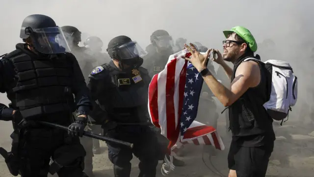 Человек с американским флагом стоит перед группой полицейских