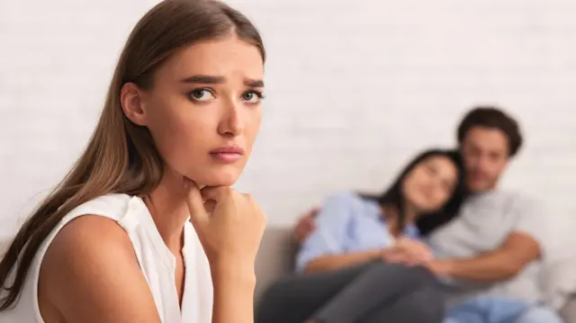 एक युवती कैमरे की ओर देख रही है जिसके पीछे धुंधले से एक कपल दिख रहे हैं