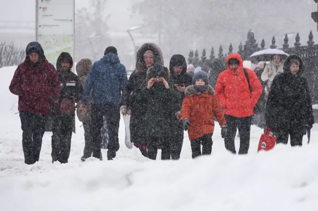 Вид из-за верхушки сугроба на идущих под снегопадом людей