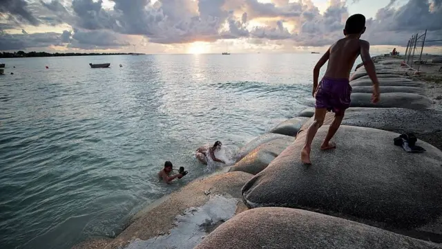 Enfants jouant dans une lagune et sur des sacs de sable pour ralentir l'avancée de la mer 