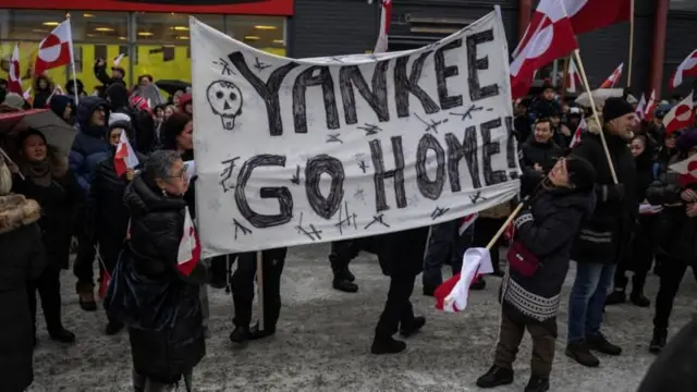 مواطنون من غرينلاند يرفعون أعلام الجزيرة ولافتة كبيرة مكتوب عليها بالأسود 