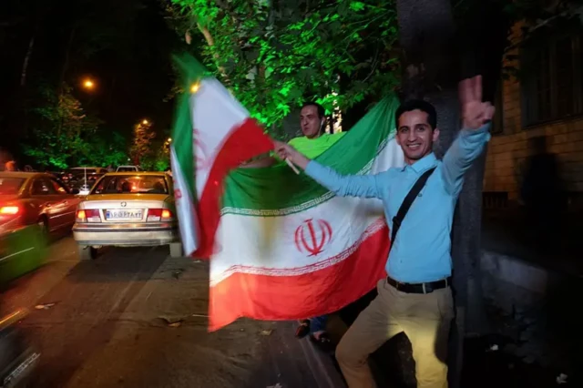 دو مرد پرچم جمهوری اسلامی را در دست گرفته‌اند و در خیابان شادمانی می‌کنند