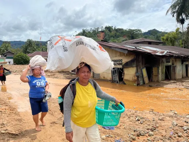 Dua perempuan sedang membawa barang-barang di Hutanabolon, salah satu kelurahan paling terdampak di Tapanuli Tengah.